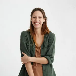 Woman with wide smile dressed in green jacket and brown t-shirt smiling broadly being happy to meet you 
